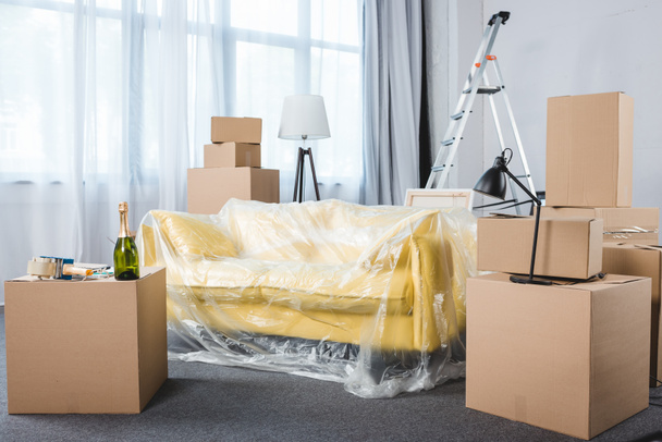 leeres Wohnzimmer mit Couch und Stapeln von Kisten während des Umzugs - Foto, Bild