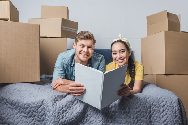 happy young couple with album relaxing in bed after moving into new home - Photo, Image