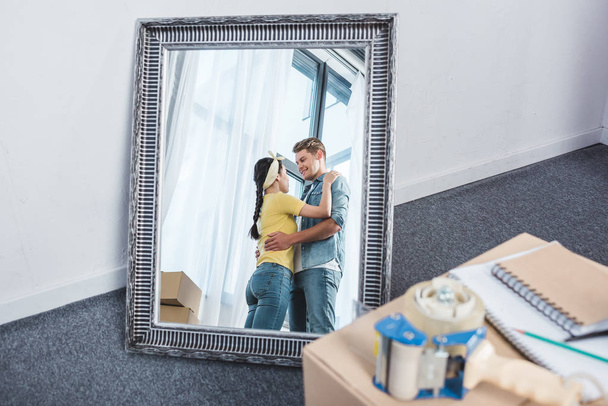 Spiegelbild eines schönen Paares, das sich nach dem Einzug in ein neues Zuhause umarmt - Foto, Bild