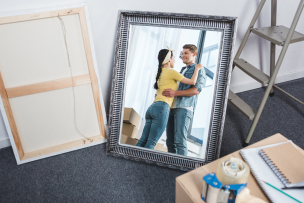 зеркальное отражение молодой пары, обнимающейся после переезда в новый дом
 - Фото, изображение