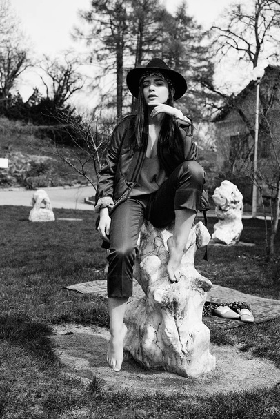 Black and white photo of stylish young woman wearing fashionable hat and posing outdoors - Valokuva, kuva