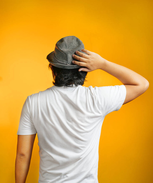 Arrière Pose de l'homme asiatique confus tenant sa tête portant Fedora chapeau sur fond jaune
 - Photo, image