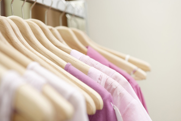 Szczegóły różowe ubrania wiszące na drewniane wieszaki w sklep odzieżowy. - Zdjęcie, obraz