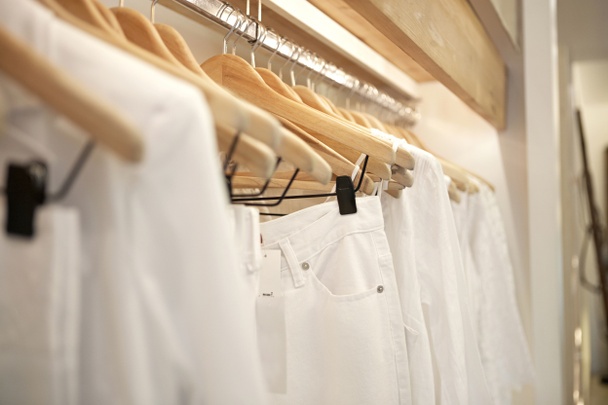 Detalle de ropa blanca colgada en perchas de madera en una tienda de moda
. - Foto, imagen