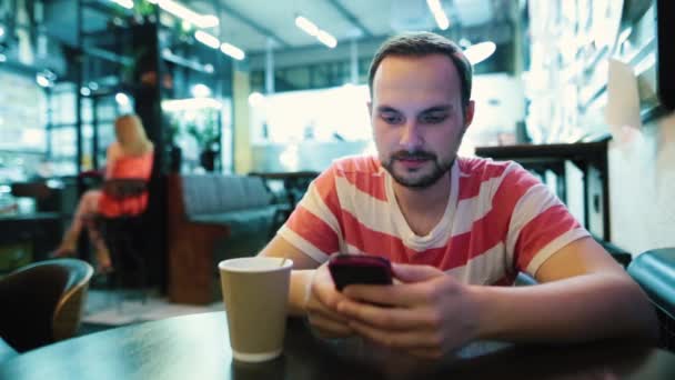 bärtiger Mann, der überrascht oder schockiert ist, wenn er auf sein Smartphone schaut. lässiger urbaner Hipster sitzt im Café. - Filmmaterial, Video