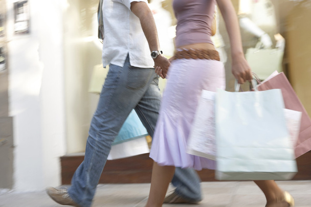 Detail of a couple walking down a shopping street with shopping bags, holding hands. - Photo, Image