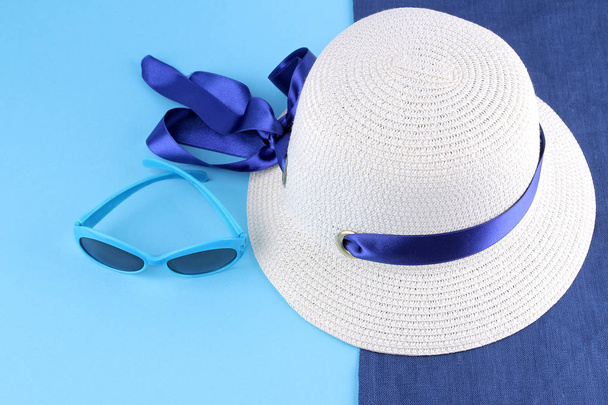 Chapeau d'été avec un ruban bleu sur une serviette bleue avec des lunettes de soleil bleues sur un fond bleu. Accessoires de plage
 - Photo, image