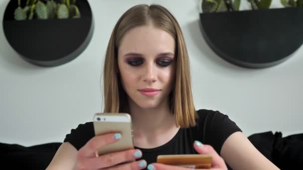 Young beautiful women texting on phone, holding card and looking in camera, smiling, black and white cafe background - Filmagem, Vídeo