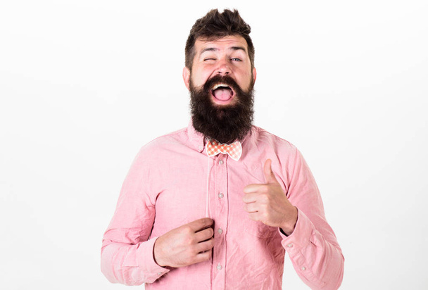 Man with stylish beard and mustache making funny face. Bearded man with happy face holding red paper bowtie, party concept. Hipster with long beard showing thumb up isolated on white background - Valokuva, kuva