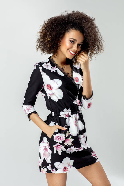 Krásná africká americká mladý ženský model nosit šaty v květiny a usmívá se - Fotografie, Obrázek