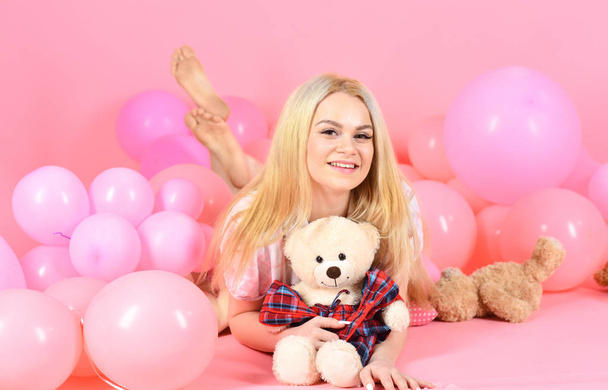 Birthday girl concept. Woman cute celebrate birthday with balloons. Girl in pajama, domestic clothes lay near air balloons, pink background. Blonde on smiling face relaxing with teddy bear toy - Foto, Imagem