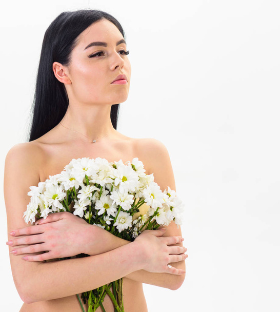 Girl on calm face naked holds chamomile flowers in front of breasts. Woman with smooth healthy skin looks attractive. Lady covers breasts with flowers, isolated on white. Natural cosmetics concept - Foto, Bild