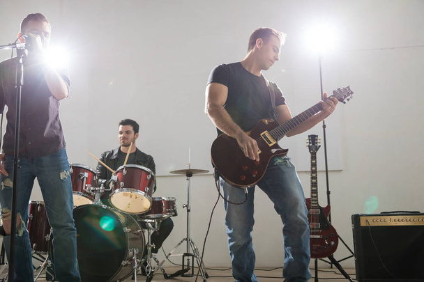 Νέοι ροκ μπάντα κιθαρίστας παίζει κιθάρα στην σκηνή με τα μέλη του συγκροτήματος σε μουσική συναυλία - Φωτογραφία, εικόνα
