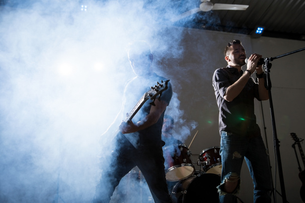 Wykonywania na scenie z gitarzysta wokalista rockowy. Jasne światło i dymu na scenie. - Zdjęcie, obraz
