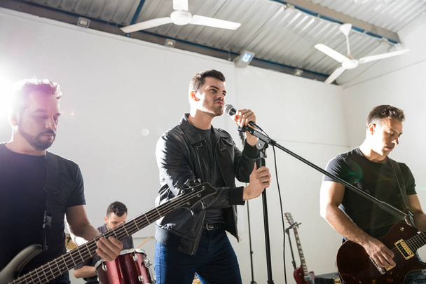 Junger Mann singt mit seinen Bandmitgliedern auf der Bühne in ein Mikrofon - Foto, Bild