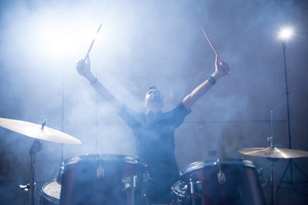 Schlagzeuger der Rockband hebt mit Licht und Rauch die Arme auf der Bühne - Foto, Bild