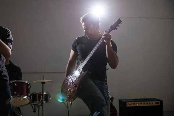 Человек играет на электрогитаре в концерте с ярким светом на сцене
 - Фото, изображение