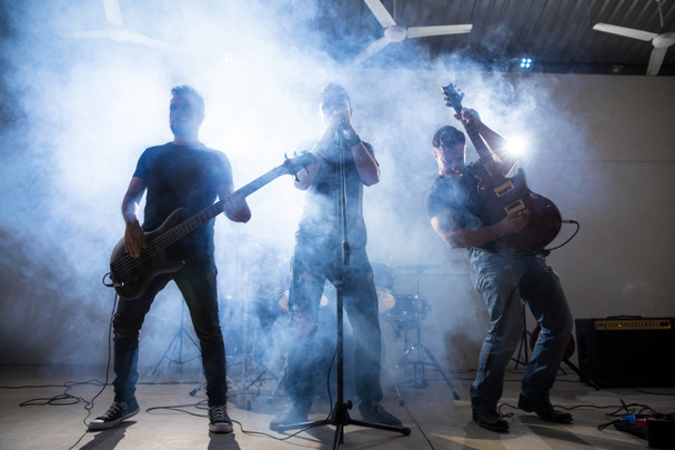Membros da banda de rock and roll se apresentando ao vivo no palco com luzes e fumaça
 - Foto, Imagem