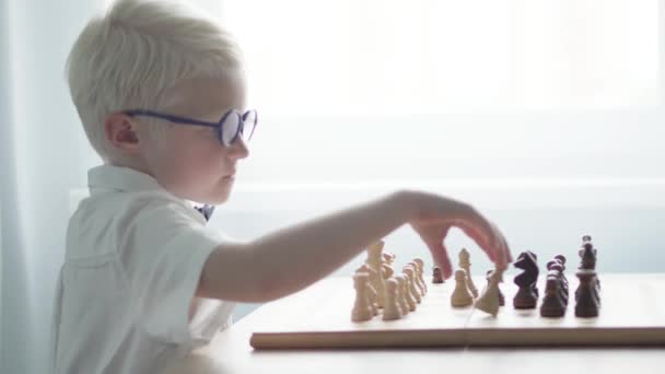 Um menino albino com uma camisa branca está jogando xadrez em uma mesa
 - Filmagem, Vídeo
