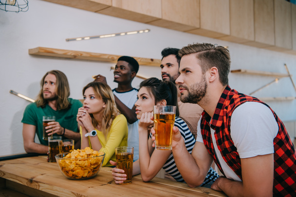  multiculturele vrienden met bier en chips kijken naar voetbal match op gericht bar  - Foto, afbeelding