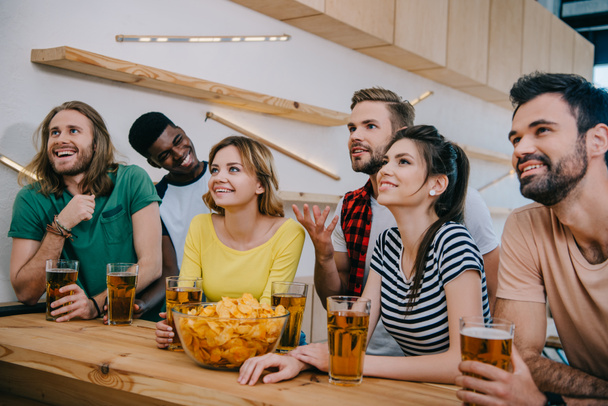 glimlachend multiculturele vrienden met bier en chips kijken naar voetbal match op balk  - Foto, afbeelding