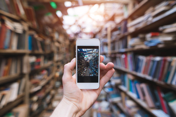 A mão humana faz uma fotografia de uma biblioteca pública em uma câmera de smartphone. Smartphone com biblioteca na tela
. - Foto, Imagem