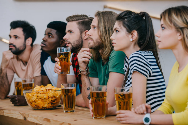 group of multicultural friends drinking beer and watching soccer match at bar  - Photo, Image