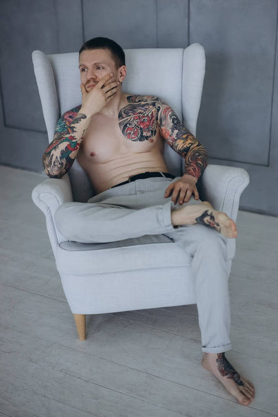 jeune homme torse nu avec des tatouages assis dans un fauteuil
 - Photo, image
