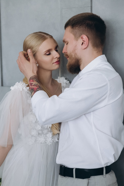 beautiful young bride and groom kissing in front of grey wall - Fotografie, Obrázek
