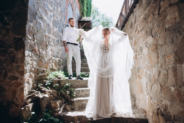 beautiful bride and handsome groom on stairs of ancient building in old town - Foto, afbeelding