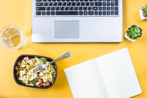 Növényi saláta makaróni sajttal tartályban tálat ebédre a Hivatal munkahelyeken közel a laptop. Felülnézet, lapos laikus - Fotó, kép