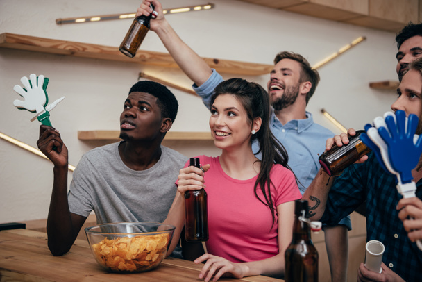 fröhliche multikulturelle Freunde feiern mit Bierflaschen und Handschlagern während des Fußballspiels an der Bar  - Foto, Bild