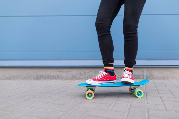 Ragazza con ragazzi rossi che cavalcano su uno skateboard blu sullo sfondo di un muro blu. Stile street. Gambe con primo piano
. - Foto, immagini