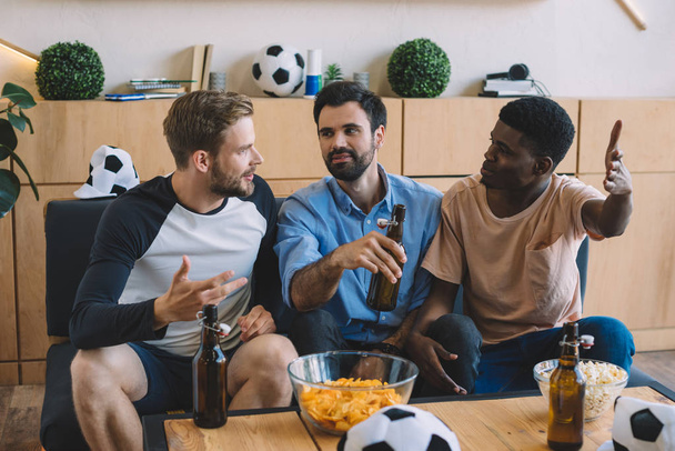 gesturing multicultural friends talking during watch of soccer match at home - 写真・画像