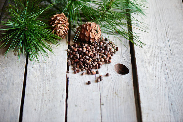 top view of green fir branch, pine nuts and cones on wooden background with copy space - Photo, image