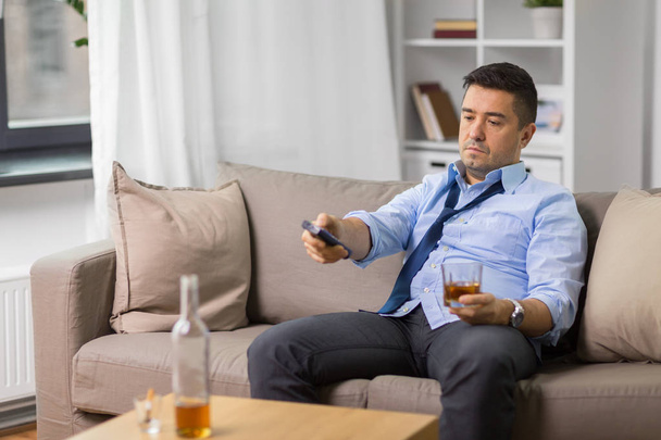drunk man with tv remote drinking alcohol at home - Foto, Imagem