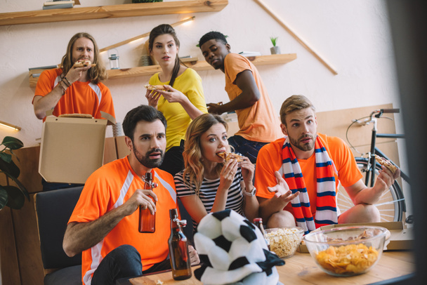 amigos multiculturais com pizza e cerveja assistindo jogo de futebol em casa
 - Foto, Imagem