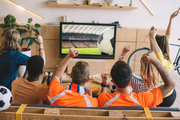 vista trasera del grupo de amigos celebrando y haciendo gestos de sí mientras están sentados en el sofá durante el reloj del partido de fútbol en casa
 - Foto, Imagen