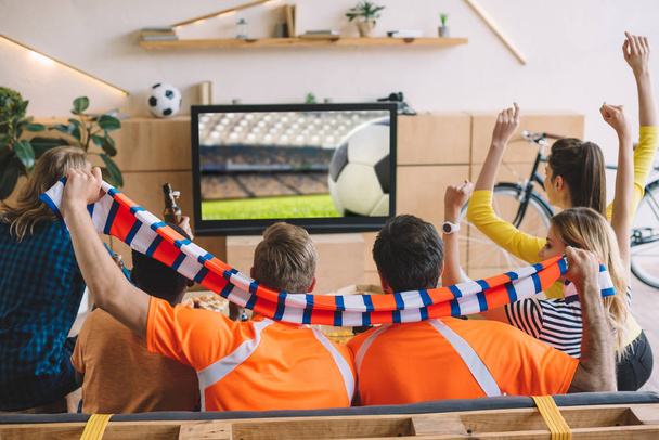 Ομάδα των οπαδών ποδοσφαίρου γιορτάζει και κάνει χειρονομίες Ναι ενώ κάθεστε στον καναπέ κατά τη διάρκεια ρολόι του αγώνα ποδοσφαίρου στο σπίτι - Φωτογραφία, εικόνα