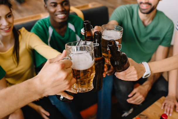 vista close-up de fãs de futebol multicultural comemorando e clinking garrafas de cerveja e copos
  - Foto, Imagem