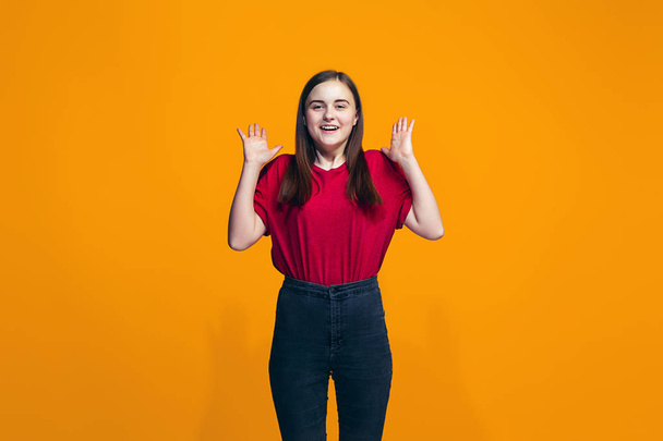 The happy teen girl standing and smiling against orange background. - Foto, imagen