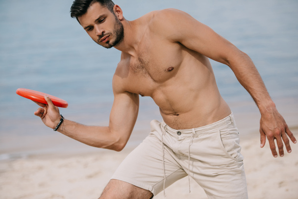 joven guapo jugando con disco volador en la playa
 - Foto, imagen