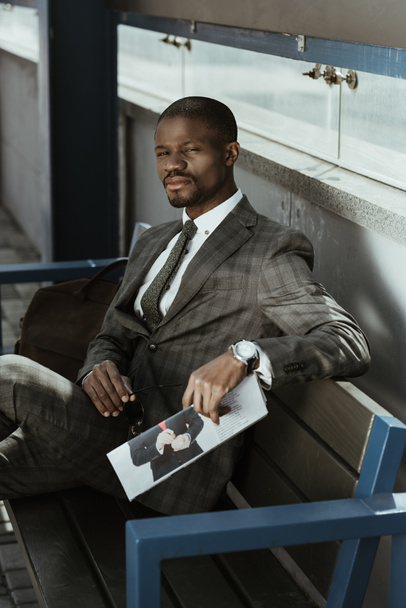 Joven empresario afroamericano sentado en el banquillo con periódico
 - Foto, Imagen