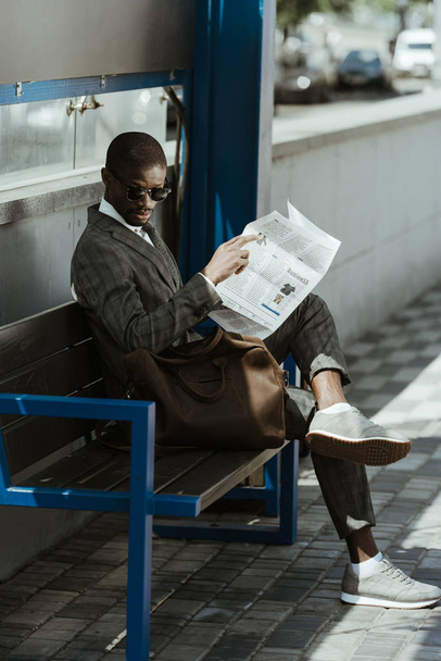 Joven hombre de negocios afroamericano con periódico descansando en la banca
 - Foto, Imagen