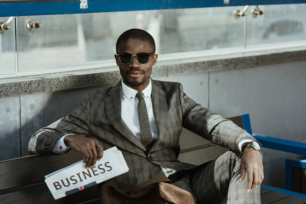 Νεαρός αφρικανική αμερικανική επιχειρηματίας σε γυαλιά ηλίου που κάθεται στον πάγκο - Φωτογραφία, εικόνα