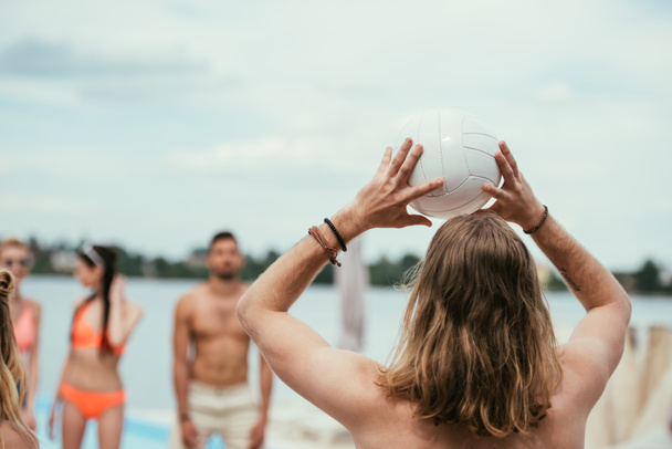 back view of young man playing volleyball with friends on beach - Fotó, kép