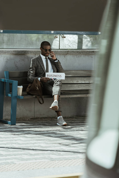 Αφρικανικός Αμερικανός επιχειρηματίας φορώντας κοστούμι και εκμετάλλευση εφημερίδα στηρίζεται σε πάγκο - Φωτογραφία, εικόνα
