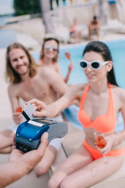 笑顔の若い女性がプールサイドで友人とシャンパンを飲みながらクレジット カードで支払い - 写真・画像