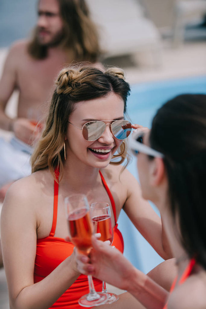 selective focus of young female friends drinking champagne and smiling at pool - Foto, Imagem