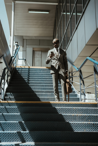 Jeune homme d'affaires afro-américain utilisant un smartphone tout en marchant dans les escaliers
 - Photo, image